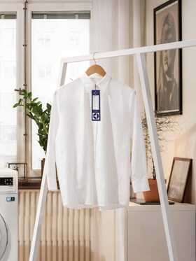 Camisa blanca con etiqueta de lavado colgada en una sala de estar