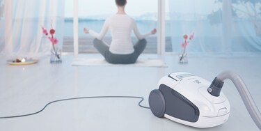 Mujer haciendo yoga con su aspiradora Electrolux Ultra Silencer en segundo plano